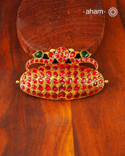 Inspired by the grandeur of traditional South Indian jewellery, this statement pendant is handcrafted in 92.5 sterling silver and finished with a rich gold polish. The design is crowned by a pair of graceful peacocks, a timeless symbol of beauty, prosperity, and auspiciousness, framing a central kundan motif.

The sculptural form is entirely adorned with hand-set ruby-toned kundan stones, creating a striking play of colour and craftsmanship. 
