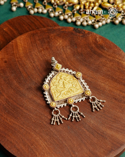 Enhance your style with the timeless elegance of the Dual Tone Silver Pendant. Handcrafted by skilled karigars in Barmer, Rajasthan, this neckpiece features traditional Bandhel work, where a thin sheet of hand beaten 22 carat gold is set on 92.5 silver using a unique wax setting technique. A classic representation of fine Indian traditional craftsmanship. 

Chain not included