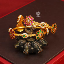 Introducing our Gold Polish Silver Bangles, crafted in silver with flawless gold polish. These beautiful bangles feature red and green alternating flowers with pearl highlights, making them the perfect complement to your classic Indian outfits. Experience the elegance and versatility of these bangles today.  Comes in a pair (2 bangles)