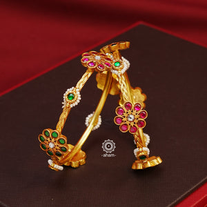 Introducing our Gold Polish Silver Bangles, crafted in silver with flawless gold polish. These beautiful bangles feature red and green alternating flowers with pearl highlights, making them the perfect complement to your classic Indian outfits. Experience the elegance and versatility of these bangles today.  Comes in a pair (2 bangles)