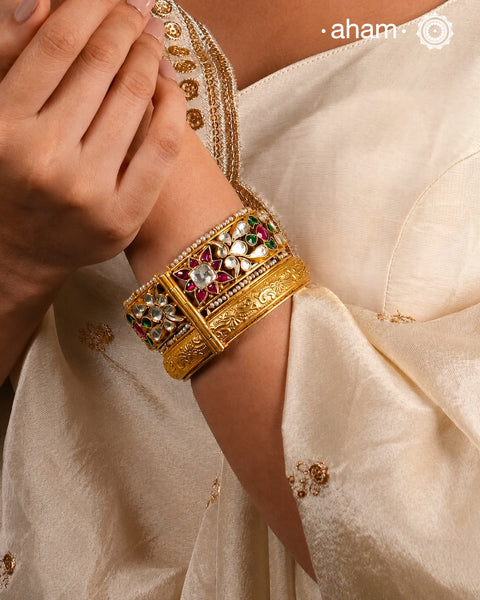 This openable Kundan Gold Polish Silver Kada gives the illusion of wearing two stacked kadas, with exquisite kundan work and laced pearls adding to its charm. Made with silver and finished in gold polish, it's a must-have for any jewellery collection.