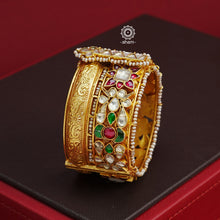 This openable Kundan Gold Polish Silver Kada gives the illusion of wearing two stacked kadas, with exquisite kundan work and laced pearls adding to its charm. Made with silver and finished in gold polish, it's a must-have for any jewellery collection.  The price is for one piece kada only.