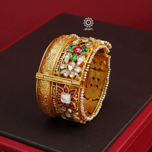 This openable Kundan Gold Polish Silver Kada gives the illusion of wearing two stacked kadas, with exquisite kundan work and laced pearls adding to its charm. Made with silver and finished in gold polish, it's a must-have for any jewellery collection.  The price is for one piece kada only.