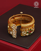 This openable Kundan Gold Polish Silver Kada gives the illusion of wearing two stacked kadas, with exquisite kundan work and laced pearls adding to its charm. Made with silver and finished in gold polish, it's a must-have for any jewellery collection.