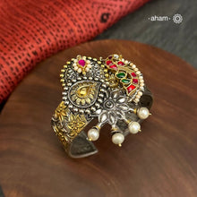 Noori two tone silver open hand cuff with a vibrant Peacock motif. An eclectic mix of elements, with a play of colours, textures, forms and workmanship. Handcrafted in 92.5 Sterling Silver with two tones that make them so versatile and unique. Modern Heirloom pieces that can be worn across generations. 
The price is for one piece kada only. 

