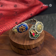 This Noori Two Tone Lapiz Stone Silver Cuff is a work of art. The braided cuff features a lapiz stone with kundan inlay on one side and a red green bird on the other, creating a classic dual tone design. Expertly crafted, this cuff is a stunning addition to any jewelry collection.
The price is for one piece kada only. 

