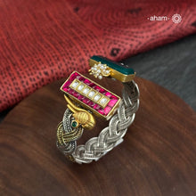 Introducing the Noori Two Tone Silver Cuff, a beautifully crafted open cuff in 92.5 silver featuring a two-tone braided band adorned with stunning green and pink kundan and parrot designs. Elevate your style with this unique and elegant piece, perfect for any occasion.

The price is for one piece kada only.