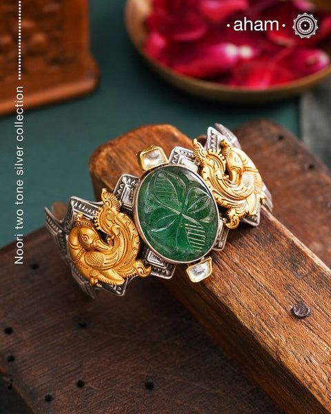 Noori two tone silver open hand cuff with a vibrant peacock motif and carved green onyx in the center. An eclectic mix of elements, with a play of colours, textures, forms and workmanship. Handcrafted in 92.5 Sterling Silver with two tones that make them so versatile and unique. Modern Heirloom pieces that can be worn across generations.
The price is for one piece kada only.