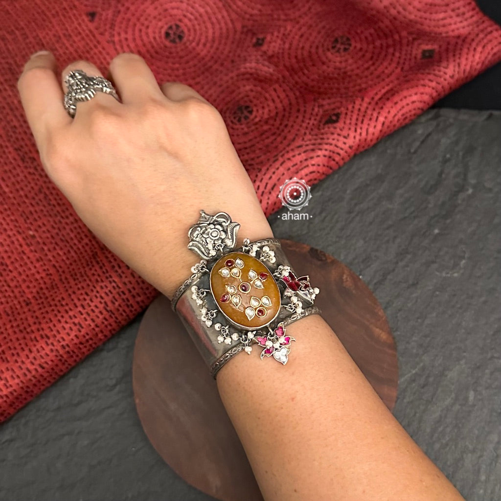 Introducing the Ira Silver HandCuff, a bold statement piece that exudes confidence. Made from 92.5 silver, it features stone work with intricate kundan inlay work and delicate pearls. Perfect for minimal accessorizing while still making a statement. Let your wrists do the talking with this chic and unique cuff.