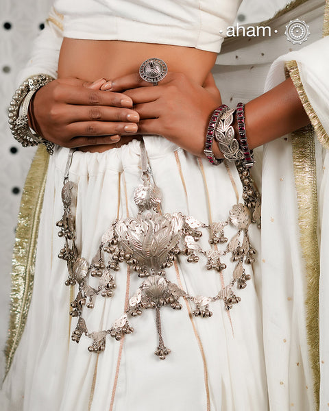 Rooted in the traditions of India's tribal communities, this handcrafted Silver Kamarbandh is a striking expression of heritage and craftsmanship. At its heart lies an intricately carved peacock motif, meticulously handcrafted using the traditional Chilai work technique, surrounded by hand-cut leaf motifs and cascading silver ghungroos. Every element comes together to create a piece that moves gracefully with every step.