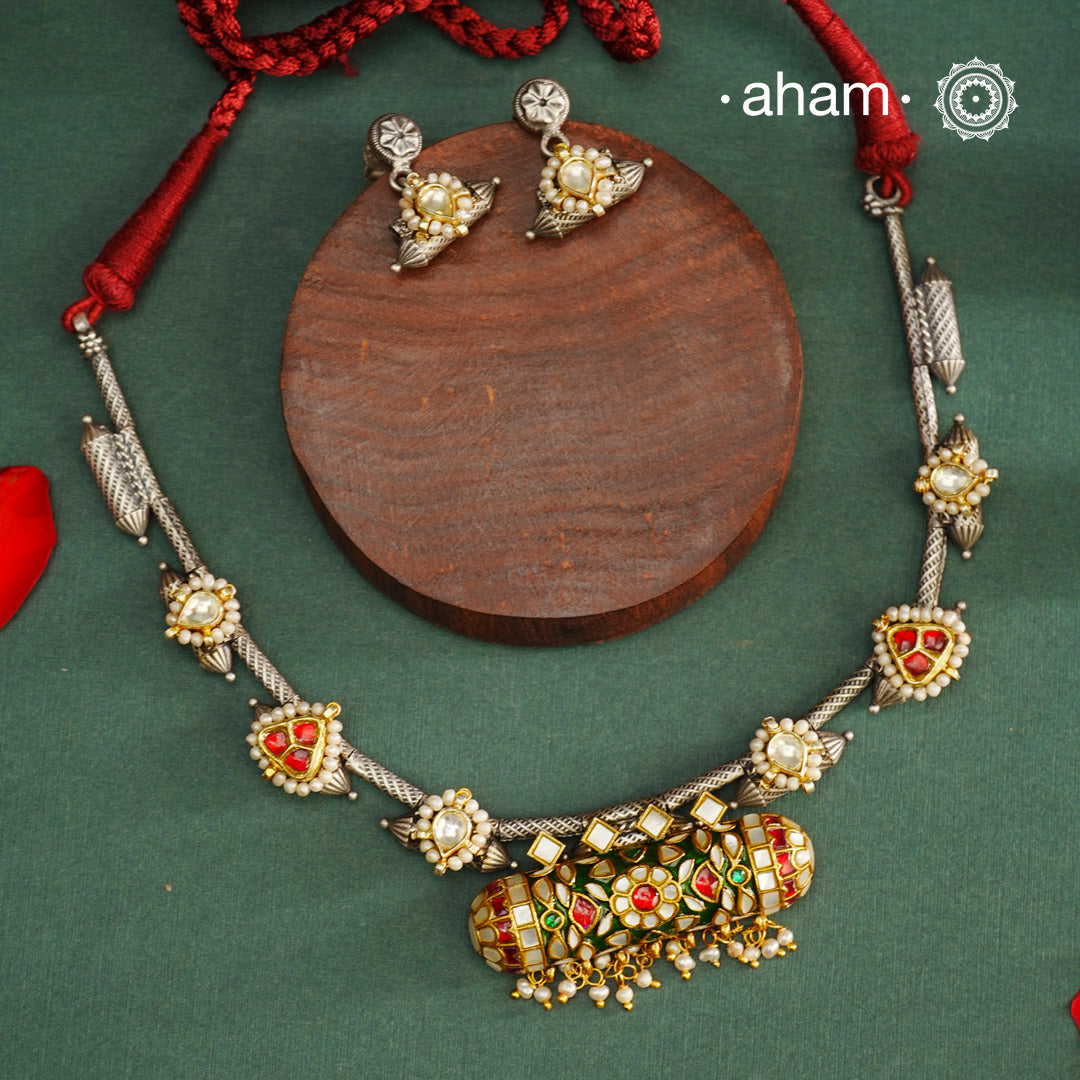 Expertly crafted in 92.5% silver, the Noori Dual Tone Silver Neckpiece & Earrings Set blends traditional South Indian amulet design with contemporary elegance. Featuring intricate kemp work and gold polish at its center, the set is adorned with multiple small silver amulets along the chain and delicate pearl highlights. This dual-tone ensemble offers a refined balance of heritage and modernity, making it a timeless addition to any collection.