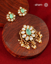 A celebration of classic craftsmanship, this pendant and earring set features a striking green center stone framed by shimmering moissanites in an intricate floral design and laced with pearls.Crafted in 92.5 silver and finished in gold polish, it is a versatile piece that effortlessly elevates festive, wedding, and occasion wear.