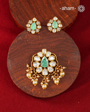 A celebration of classic craftsmanship, this pendant and earring set features a striking green center stone framed by shimmering moissanites in an intricate floral design and laced with pearls.Crafted in 92.5 silver and finished in gold polish, it is a versatile piece that effortlessly elevates festive, wedding, and occasion wear.