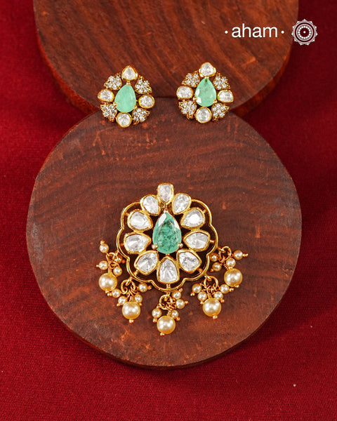 A celebration of classic craftsmanship, this pendant and earring set features a striking green center stone framed by shimmering moissanites in an intricate floral design and laced with pearls.Crafted in 92.5 silver and finished in gold polish, it is a versatile piece that effortlessly elevates festive, wedding, and occasion wear.