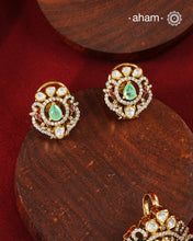 A celebration of classic craftsmanship, this pendant and earring set features a striking green center stone framed by shimmering moissanites in an intricate floral design and laced with pearls.Crafted in 92.5 silver and finished in gold polish, it is a versatile piece that effortlessly elevates festive, wedding, and occasion wear.