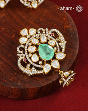 A celebration of classic craftsmanship, this pendant and earring set features a striking green center stone framed by shimmering moissanites in an intricate floral design and laced with pearls.Crafted in 92.5 silver and finished in gold polish, it is a versatile piece that effortlessly elevates festive, wedding, and occasion wear.