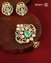 A celebration of classic craftsmanship, this pendant and earring set features a striking green center stone framed by shimmering moissanites in an intricate floral design and laced with pearls.Crafted in 92.5 silver and finished in gold polish, it is a versatile piece that effortlessly elevates festive, wedding, and occasion wear.
