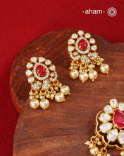 A celebration of classic craftsmanship, this pendant and earring set features a striking ruby-hued center stone framed by shimmering moissanites in an intricate floral design and laced with pearls.Crafted in 92.5 silver and finished in gold polish, it is a versatile piece that effortlessly elevates festive, wedding, and occasion wear.
