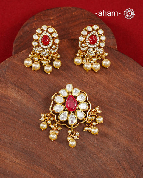 A celebration of classic craftsmanship, this pendant and earring set features a striking ruby-hued center stone framed by shimmering moissanites in an intricate floral design and laced with pearls.Crafted in 92.5 silver and finished in gold polish, it is a versatile piece that effortlessly elevates festive, wedding, and occasion wear.