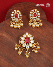 A celebration of classic craftsmanship, this pendant and earring set features a striking ruby-hued center stone framed by shimmering moissanites in an intricate floral design and laced with pearls.Crafted in 92.5 silver and finished in gold polish, it is a versatile piece that effortlessly elevates festive, wedding, and occasion wear.