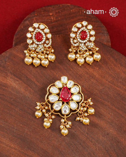 A celebration of classic craftsmanship, this pendant and earring set features a striking ruby-hued center stone framed by shimmering moissanites in an intricate floral design and laced with pearls.Crafted in 92.5 silver and finished in gold polish, it is a versatile piece that effortlessly elevates festive, wedding, and occasion wear.