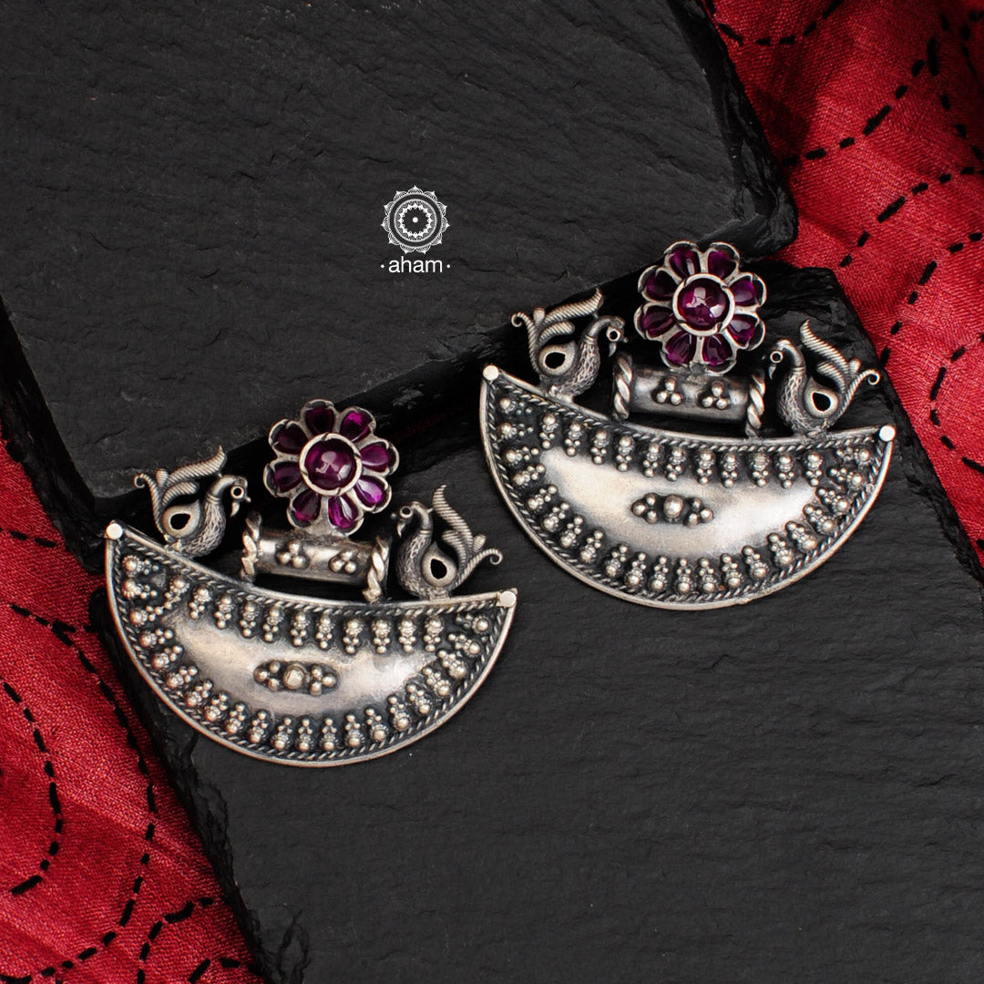 Shivneri crescent earrings with intricate rava work. Handcrafted in 92.5 sterling silver with elegant peacock motifs and maroon stone flower highlight.  