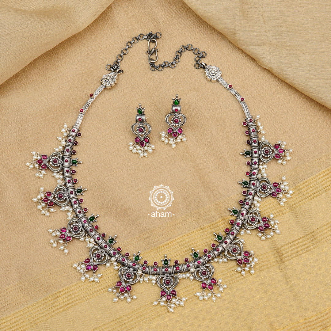 Make a sophisticated style statement this festive season in this nrityam heart shaped neckpiece and earring set. Handcrafted in 92.5 sterling silver using traditional artistry with green and maroon Kemp stone setting. Perfect for intimate weddings and upcoming festive celebrations. 