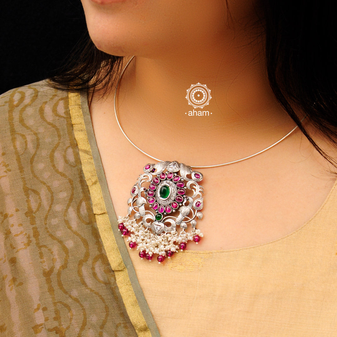 Flaunt this beautiful Nrityam hasli with elegant flower pendant with dangling cultured pearls. Beautiful, handcrafted 92.5 sterling silver neckpiece with double peacock motif and intricate floral motif with green and maroon kemp stone setting. The pendant and hasli are removable and you can wear them with other pieces of jewellery as well.  This piece strikes the perfect balance of tradition and new age simplicity. 