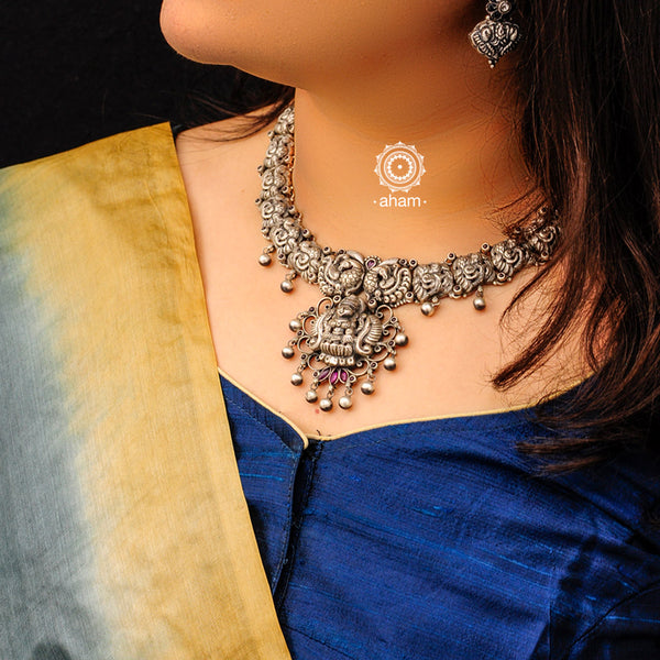 Goddess Lakshmi neckpiece handcrafted in 92.5 silver with Nakshi work. The necklace has intricate peacock motifs enhanced with maroon kemp stones. The motifs and patterns are inspired from traditional temple architecture. 