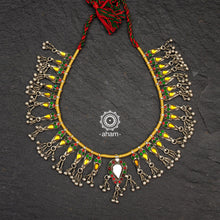 Handcrafted tribal glass silver neckpiece with statement ghungroos. Created by threading together multiple tribal pieces with green amd red stones giving it a vibrant look. This necklace truly exemplifies the continuity of the traditional designs. 