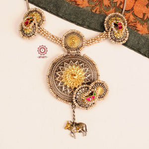 Handcrafted with love this noori dual tone neckpiece is a meticulous mix of royalty and artistry. A statement piece with cultured pearls embellished around silver floral studs, motifs with rani pink and green kundan work, and Kamadhenu (an auspicious sacred cow in the Hindu mythology) motif in the center. 