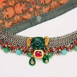 Dual tone short neckpiece with elegant peacock motif in maroon kemp setting. A meticulous mix of royalty and artistry, handcrafted in 92.5 sterling silver with a beautiful semi precious stone drop. Perfect for intimate family gatherings and festivities.