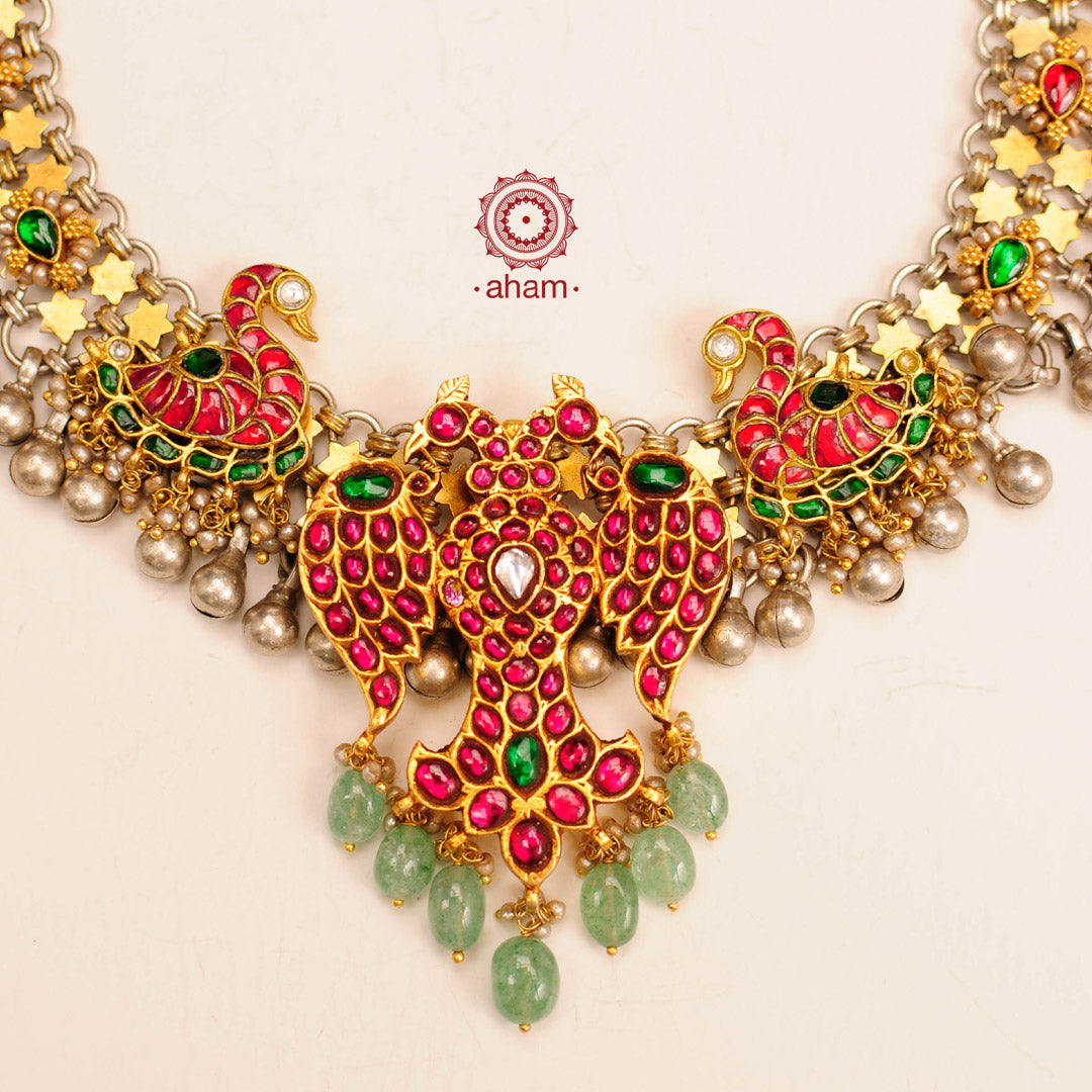 Noori two tone short neckpiece with an elegant motif of Gandaberunda (a two headed bird in hindu mythology). A meticulous mix of royalty and artistry with beautiful swan motifs, rani pink & red kundan work. Handcrafted in 92.5 sterling silver with green semi precious beads and dangling ghungroos. Perfect for intimate family gatherings and festivities.
