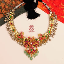 Noori two tone short neckpiece with an elegant motif of Gandaberunda (a two headed bird in hindu mythology). A meticulous mix of royalty and artistry with beautiful swan motifs, rani pink & red kundan work. Handcrafted in 92.5 sterling silver with green semi precious beads and dangling ghungroos. Perfect for intimate family gatherings and festivities.
