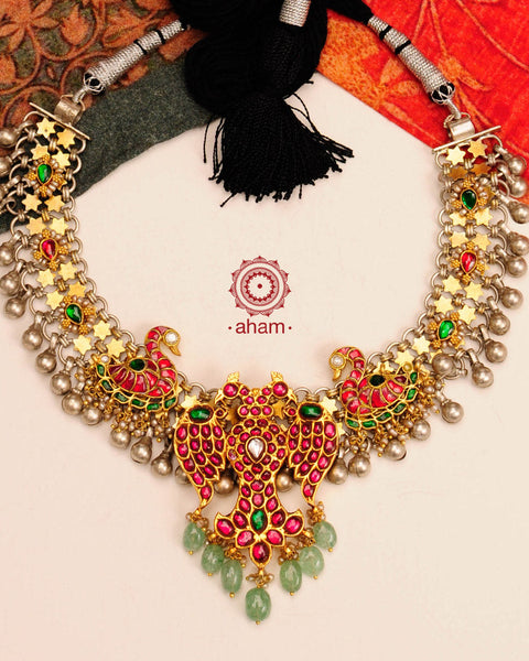 Noori two tone short neckpiece with an elegant motif of Gandaberunda (a two headed bird in hindu mythology). A meticulous mix of royalty and artistry with beautiful swan motifs, rani pink & red kundan work. Handcrafted in 92.5 sterling silver with green semi precious beads and dangling ghungroos. Perfect for intimate family gatherings and festivities.