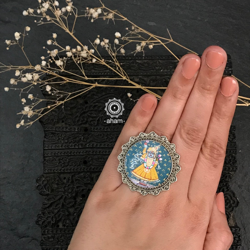 92.5 Sterling silver ring with an intricate hand painted Krishna motif in vibrant colours, enclosed with a glass top and an adjustable ring band. These are one of a kind miniature Pichwai work wearable art pieces. 