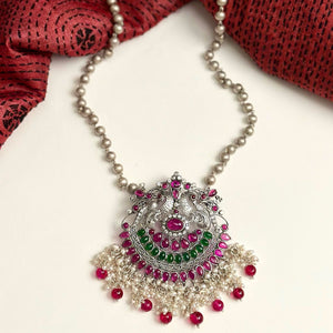 Dazzle up your look in this Nrityam double peacock neckpiece with green & maroon kemp stone setting. Handcrafted with love in 92.5 sterling silver with long silver ball chain and dangling cultured pearls. Looks fabulous with any outfit. 